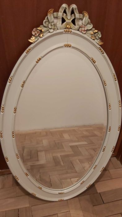 Espelho biselado com moldura de madeira com detalhes esculpidos.