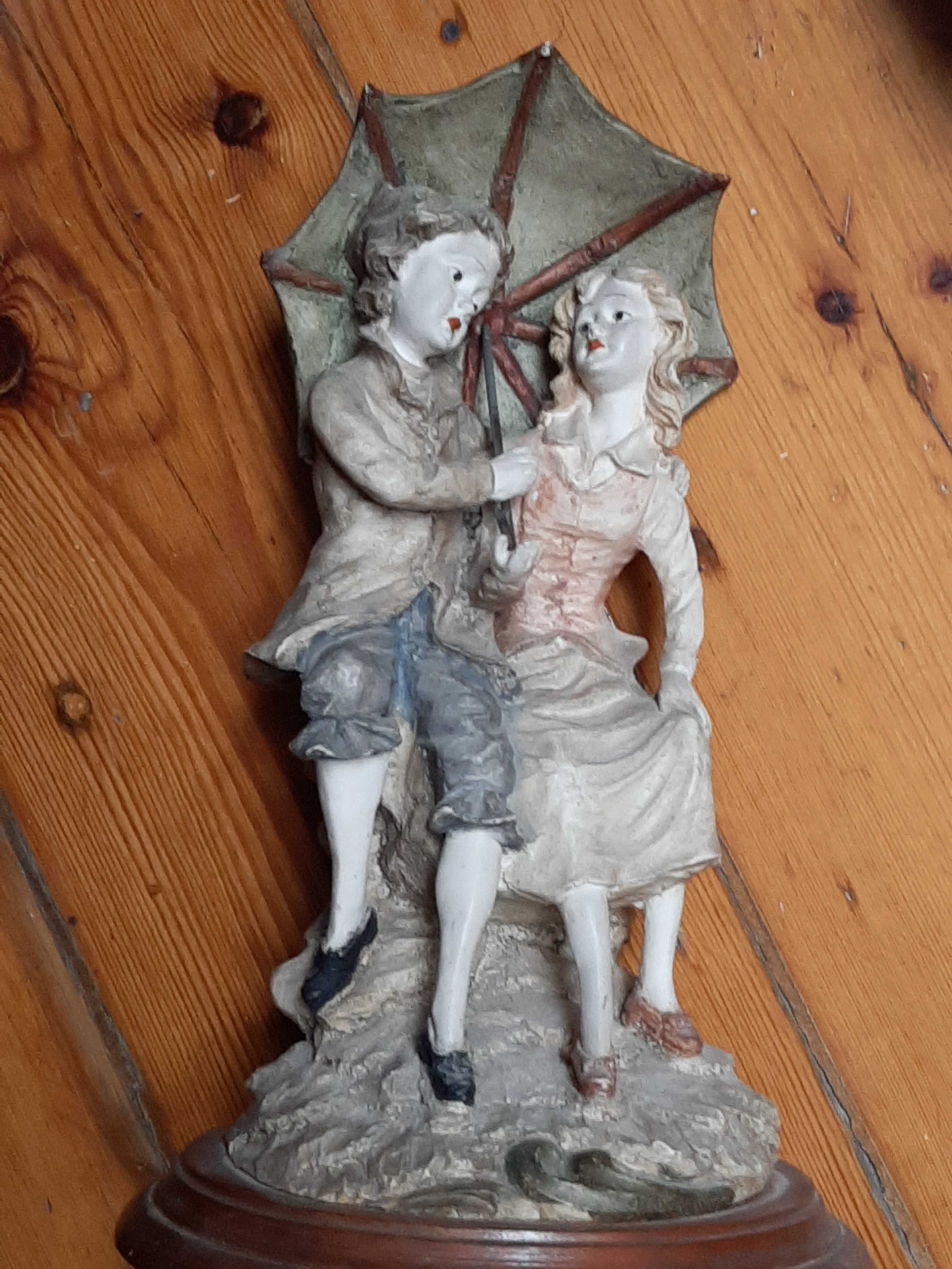 Escultura antiga de dois namorados com chapéu de chuva.