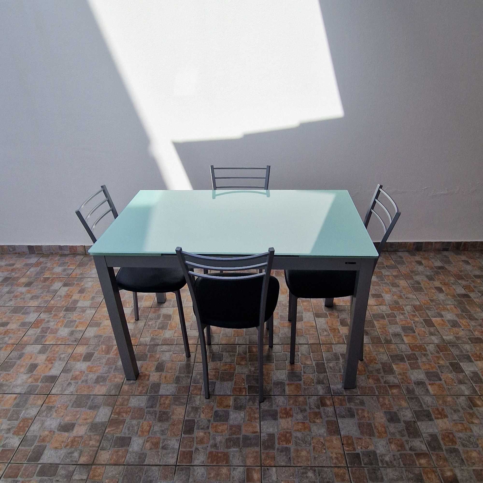 Mesa extensível com tampo em vidro e quatro cadeiras forradas a preto.