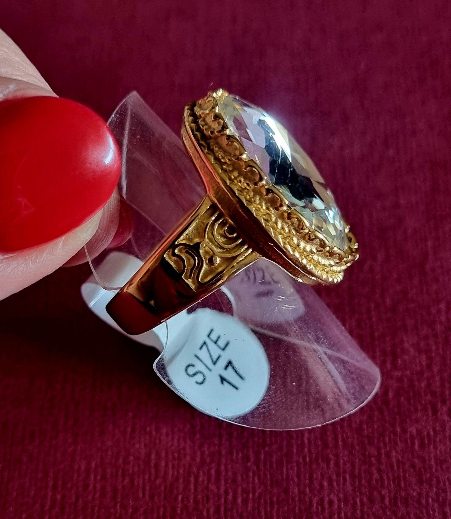 Anel dourado, em aço, com grande pedra de vidro transparente oval. T17