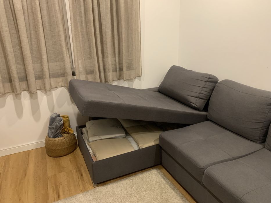 Sofa cama cinza com arrumaçao e dois bancos.