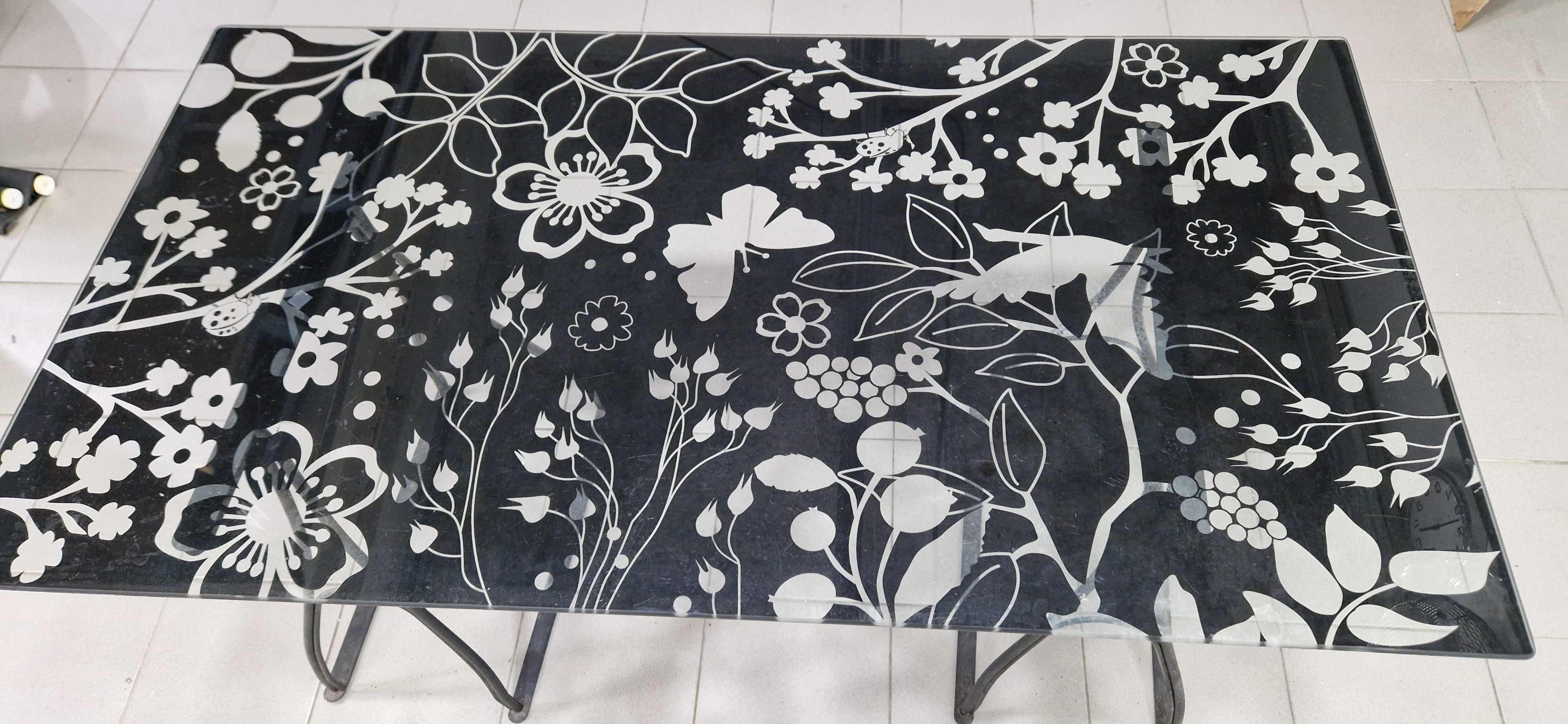 Mesa com tampo de vidro preto e padrão floral.