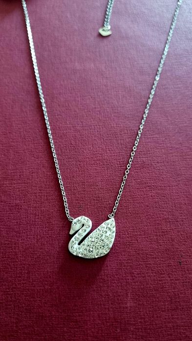 Colar prateado, em aço, com pingente em forma de cisne branco.
