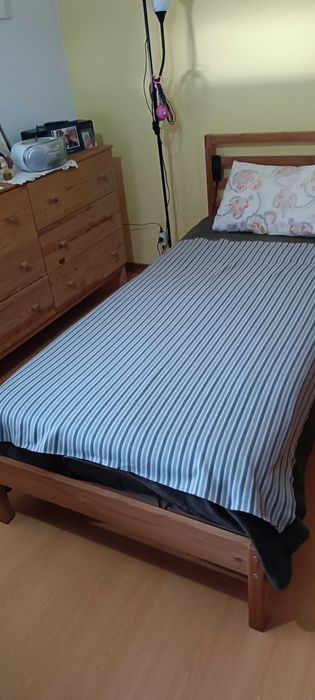 Cama de solteiro com mesa de cabeceira, cômoda e espelho de parede.