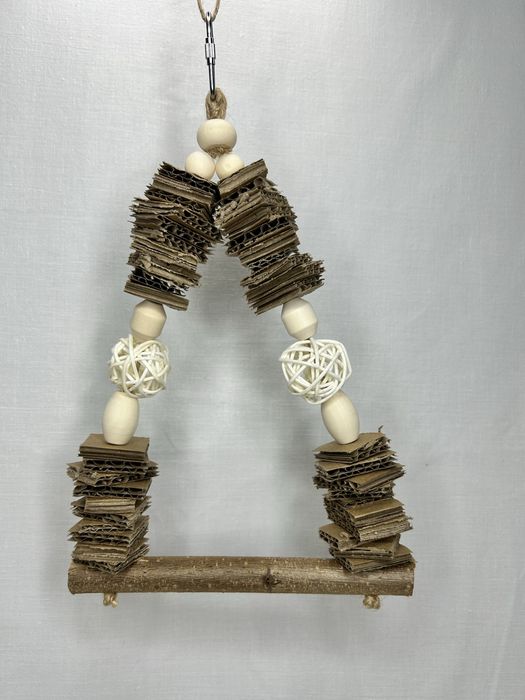 Mała huśtawka dla ptaków z tekturą i kulami wiklinowymi.