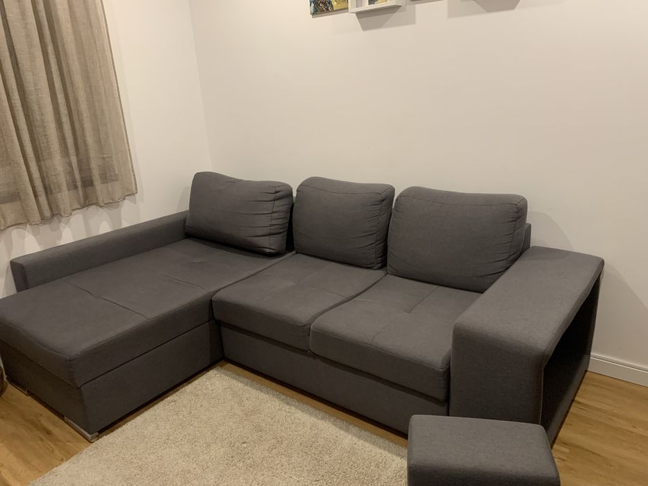 Sofa cama cinza com arrumaçao e dois bancos.
