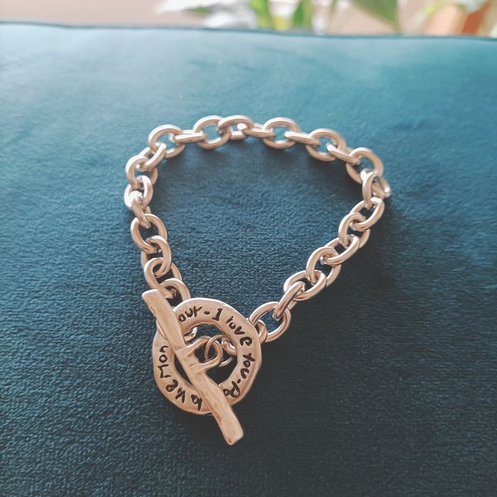 Pulseira em aço prateado com fecho com inscrição.