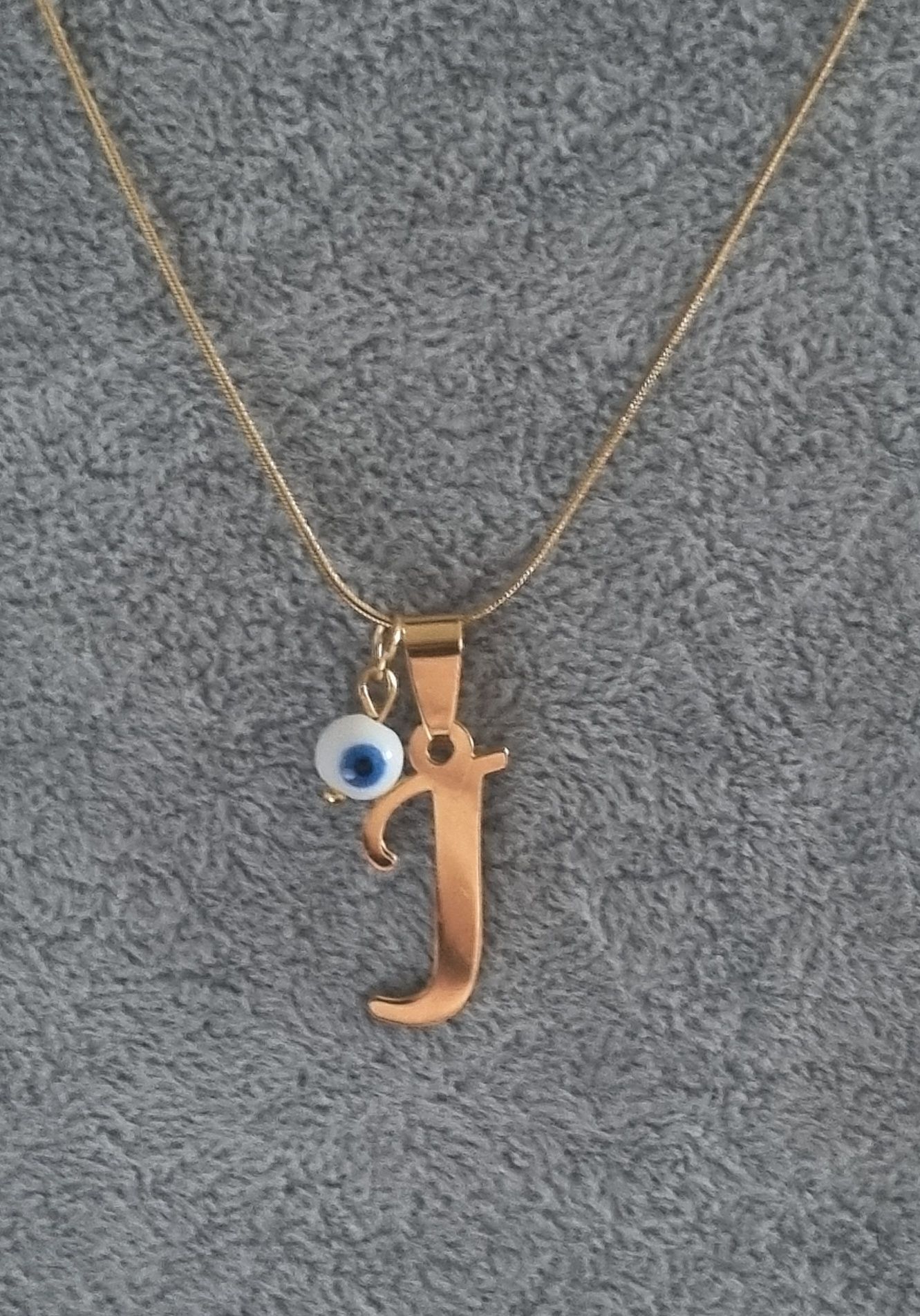 Colar dourado, em aço, com a letra "J" e olho turco. Tem extensor