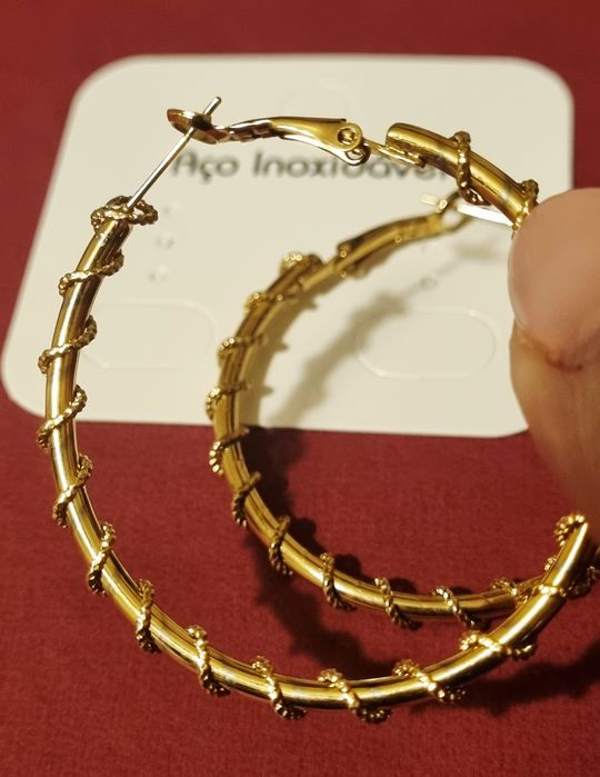 Brincos/argolas douradas, em aço, com cerca de 5cm de comprimento.