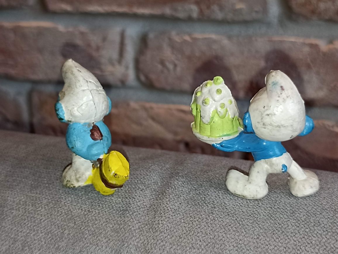 Dwie figurki smerfów z czasów PRL. Smurf z tortem i smurf z młotem.