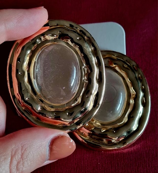 Brincos grandes dourados com acrílico oval transparente no centro.