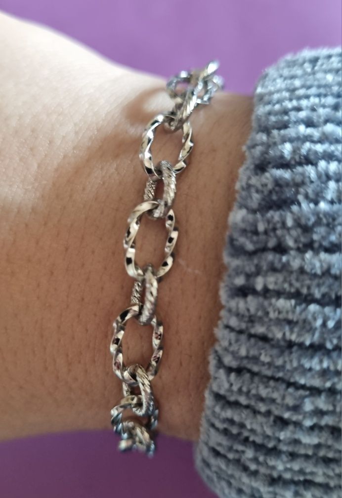 Pulseira prateada, em aço, com elos trabalhados. Tem extensor