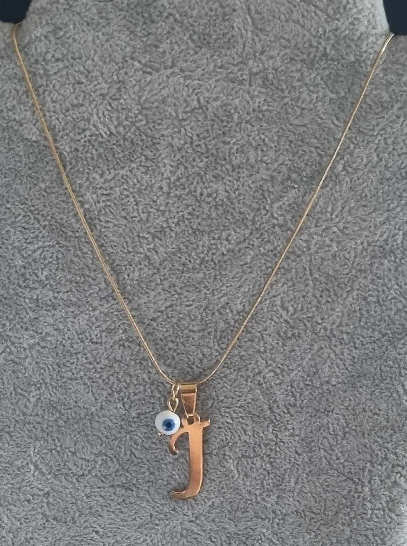 Colar dourado, em aço, com a letra "J" e olho turco. Tem extensor