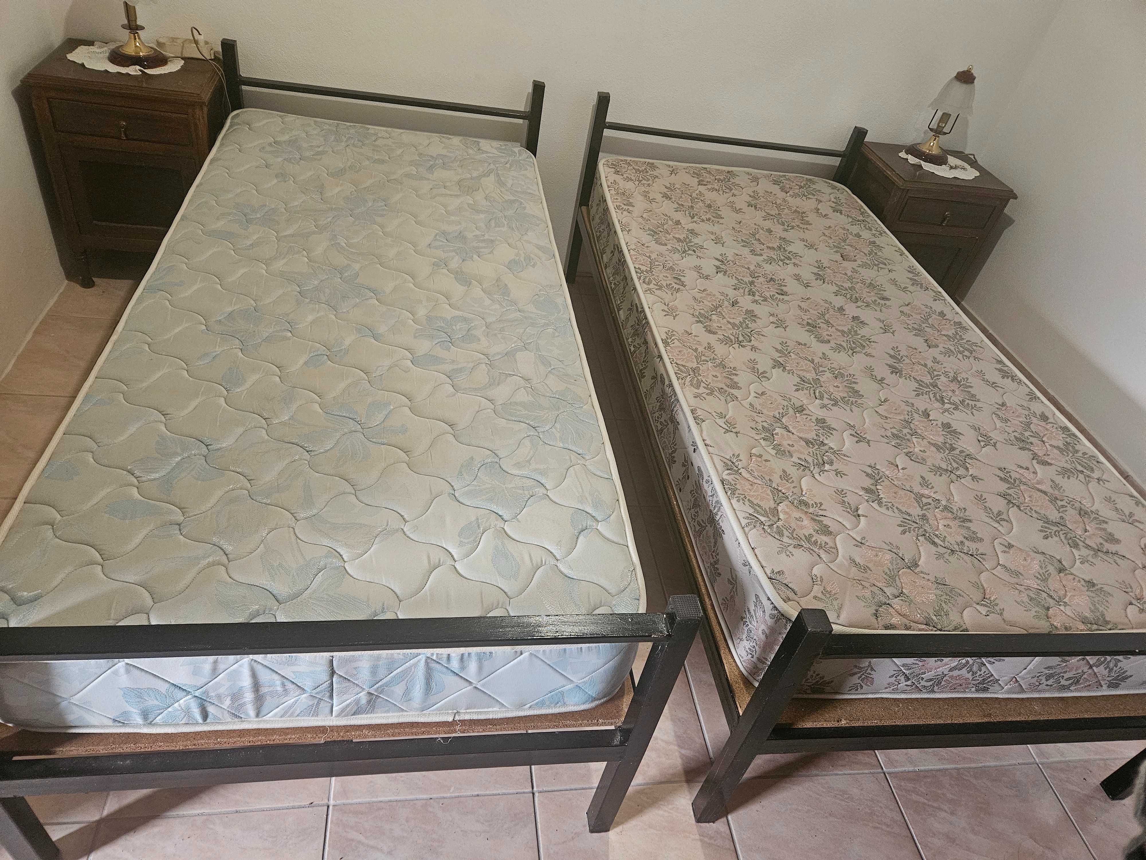 Camas de ferro com colchão e estrado.