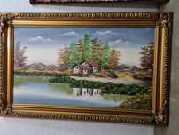Quadro com pintura de paisagem e moldura trabalhada em tom dourado.