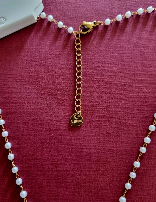Colar dourado, em aço, em forma de terço com pequenas pérolas.