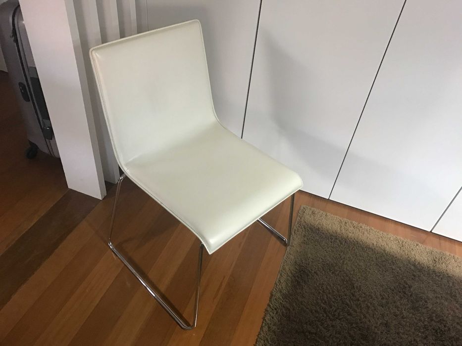 quatro cadeiras de pele branca e base em inox