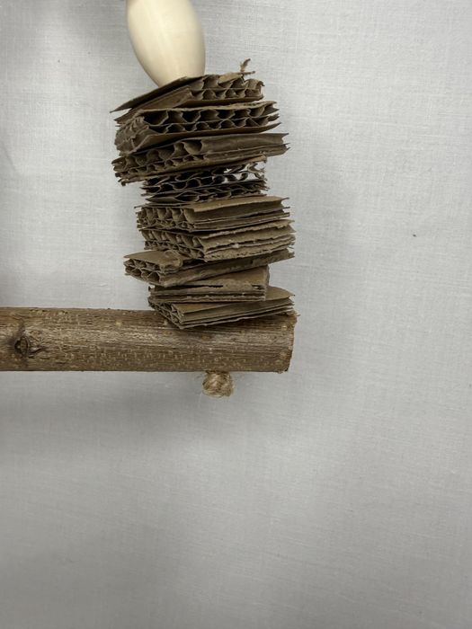 Mała huśtawka dla ptaków z tekturą i kulami wiklinowymi.