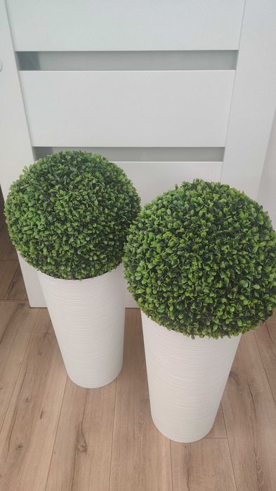 Dwie wysokie doniczki z kulami sztucznego bukszpanu.