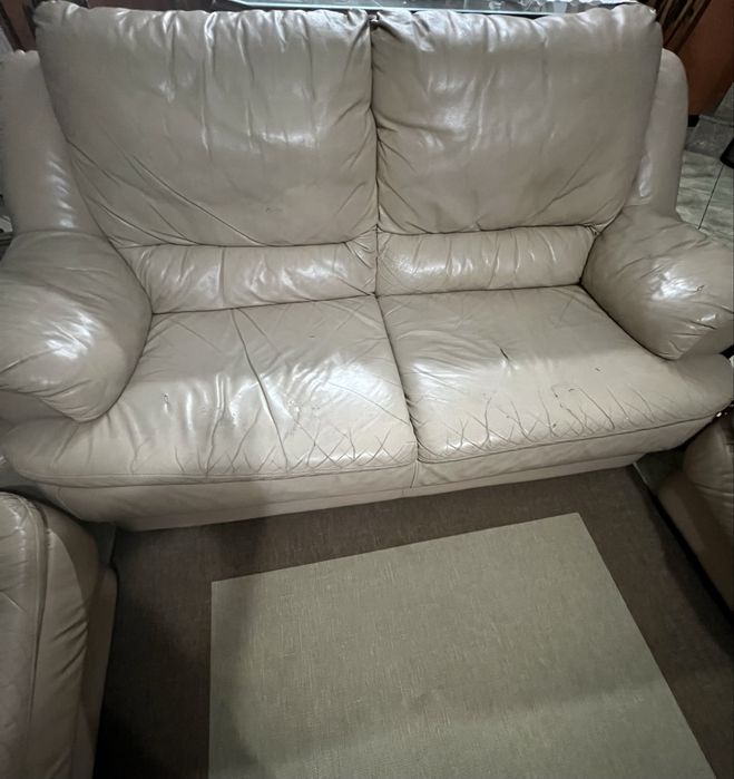Sofá  em pele , na cor bege , com alguns desgastes  pelo uso .