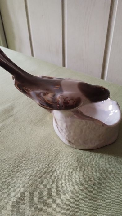 Porcelanowa figurka sroki na krawędzi podstawy.