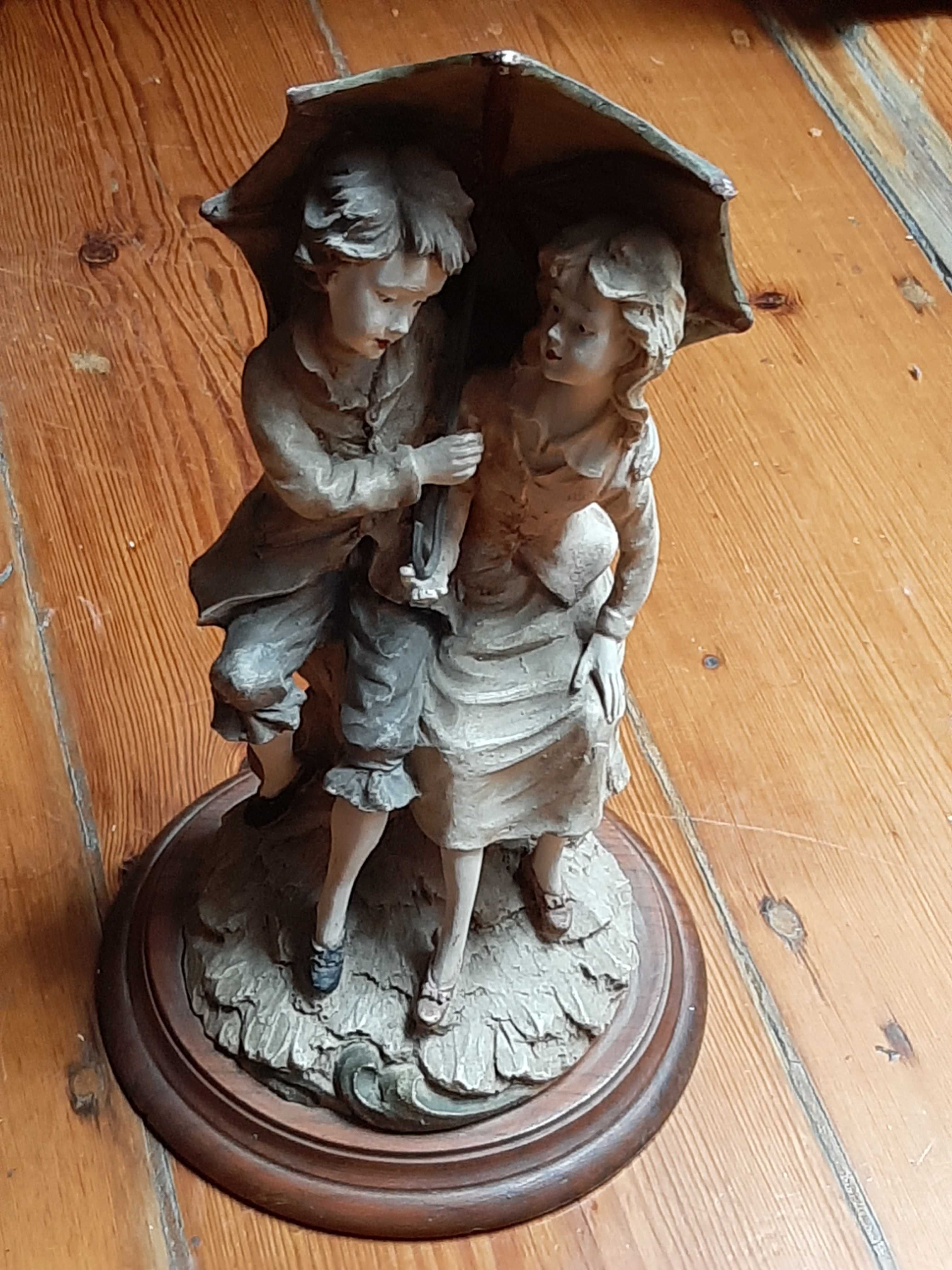 Escultura antiga de dois namorados com chapéu de chuva.