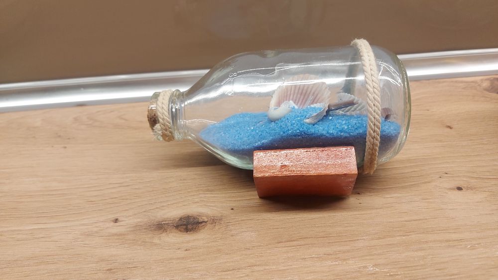 Pamiatka z nad morza, butelka z niebieskim piaskiem I muszelkami