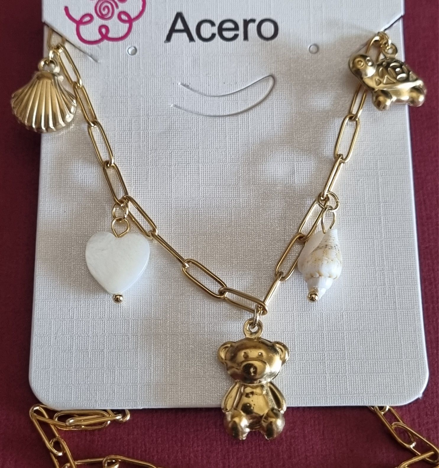 Colar dourado, em aço, com 5 pingentes diferentes. Tem extensor