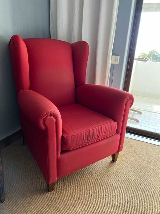 Cadeirão de orelhas forrado com tecido vermelho.