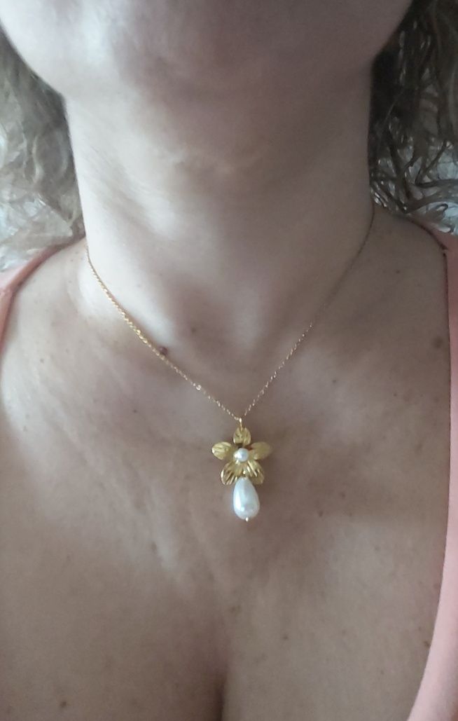 Colar dourado, em aço, com flor e pérolas. Tem extensor