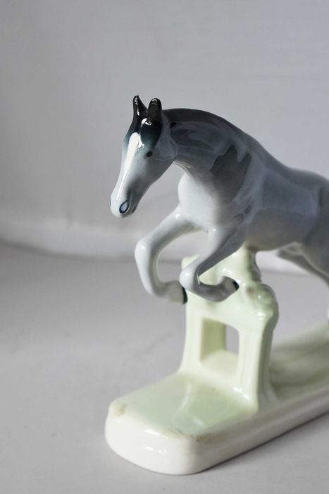 Porcelanowa figurka konia skaczącego przez przeszkodę. Chodzież