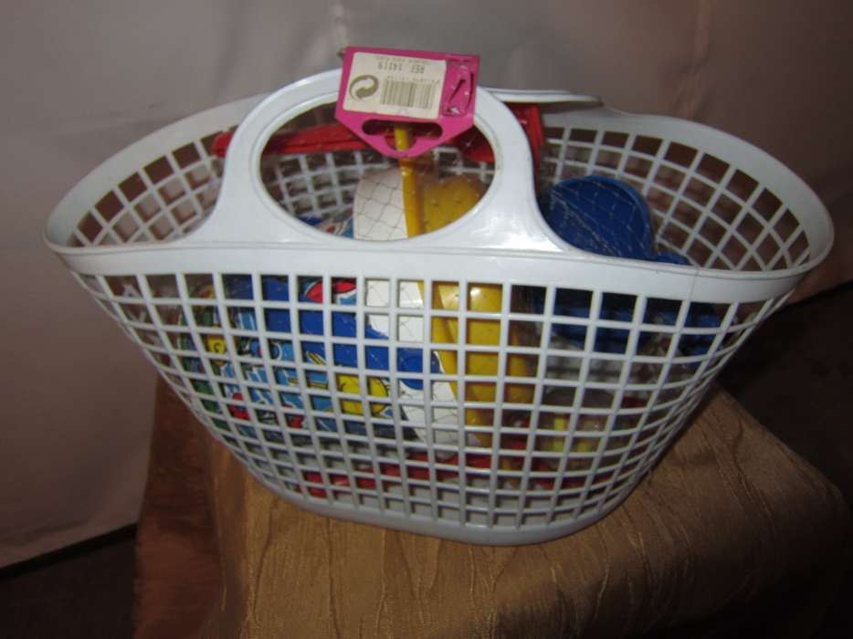 Conjunto de brinquedos de praia numa cesta branca com balde, pá, ancin