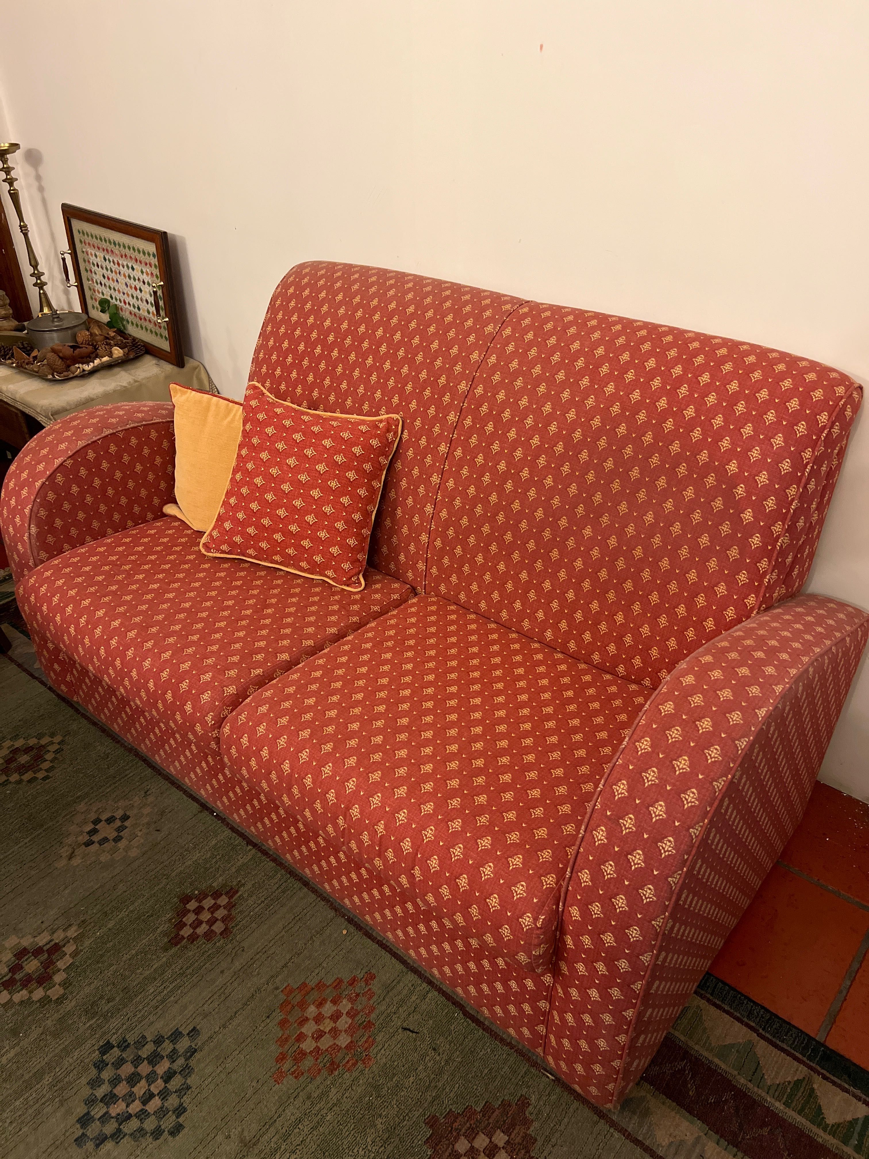 Sofá vermelho, com detalhes em amarelo e duas almofadas