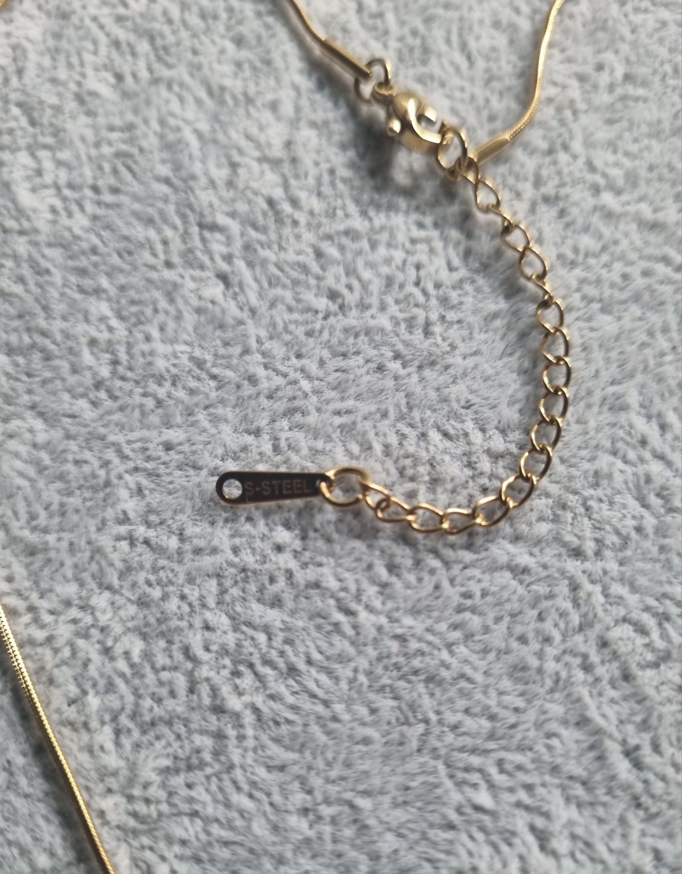 Colar dourado, em aço, com a letra "J" e olho turco. Tem extensor