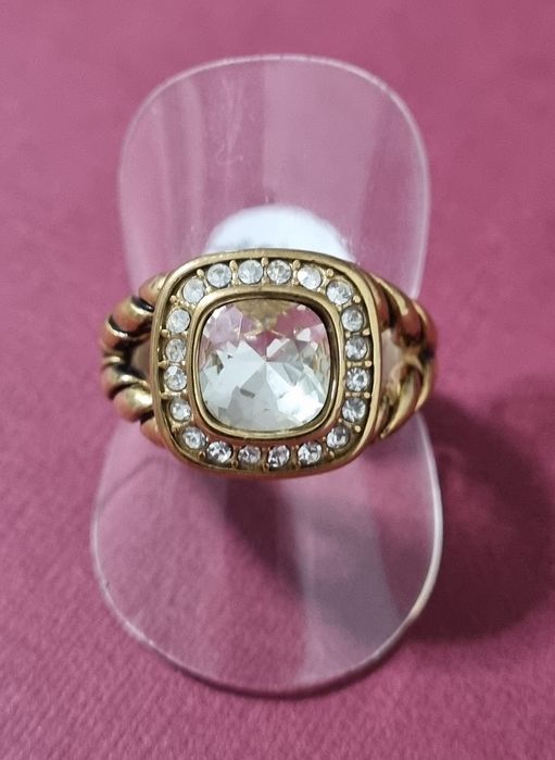 Anel dourado, em aço, com ponto de luz quadrado facetado e zirconias.