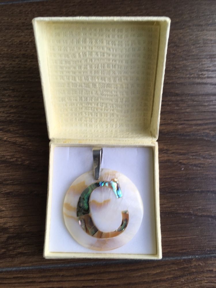 Medalha de prata e madrepérola, com a letra C.