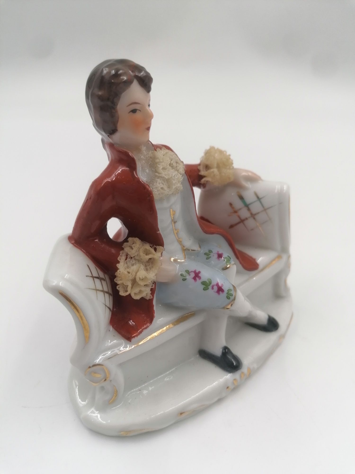 Ciekawa porcelanowa figurka panicza na sofie