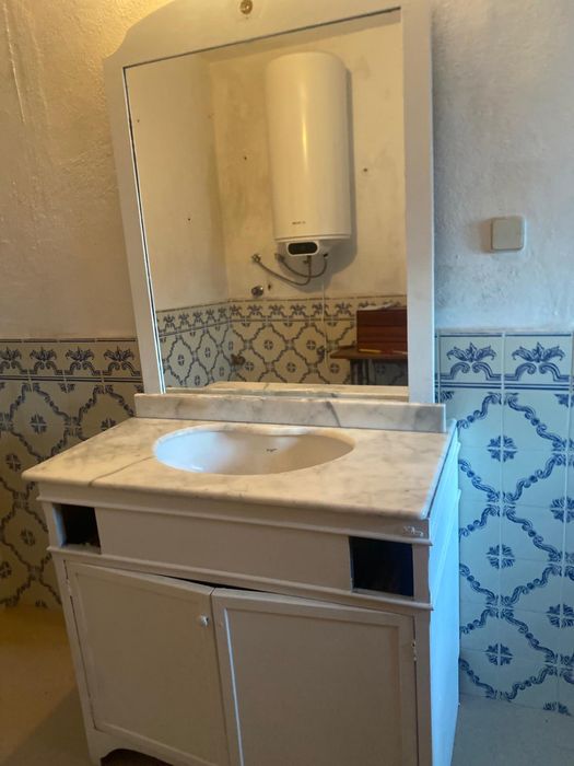 Móvle de casa de banho com tampo em mármore e espelho grande.