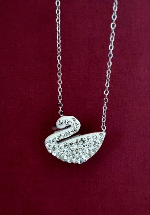 Colar prateado, em aço, com pingente em forma de cisne branco.