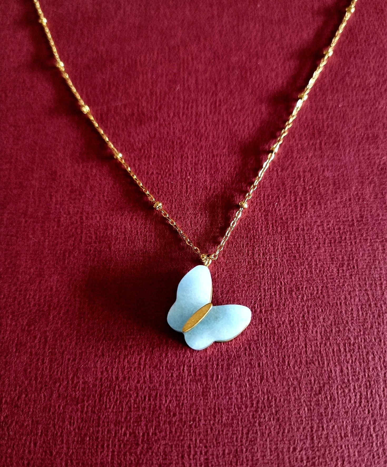 Colar dourado, em aço, malha com bolinhas e pingente borboleta azul.