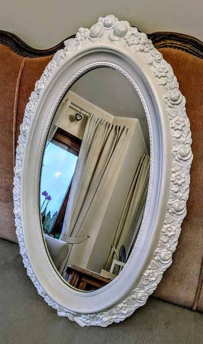 Owalne lustro w białej ramie.