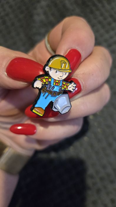 Przypinka robotnik z nogą w wiadrze.
