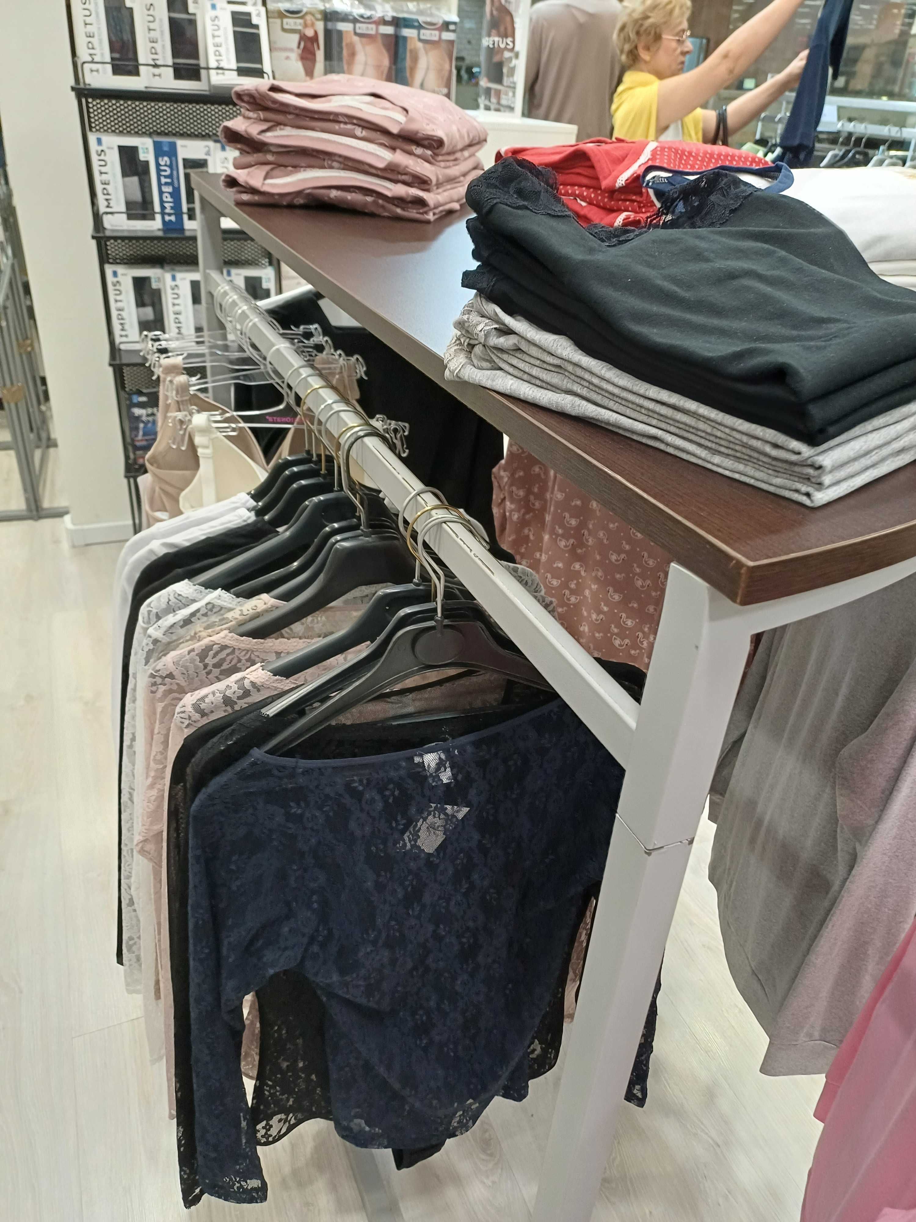 Expositor de roupa cinza com tampo em wengue, em formato de meia lua.