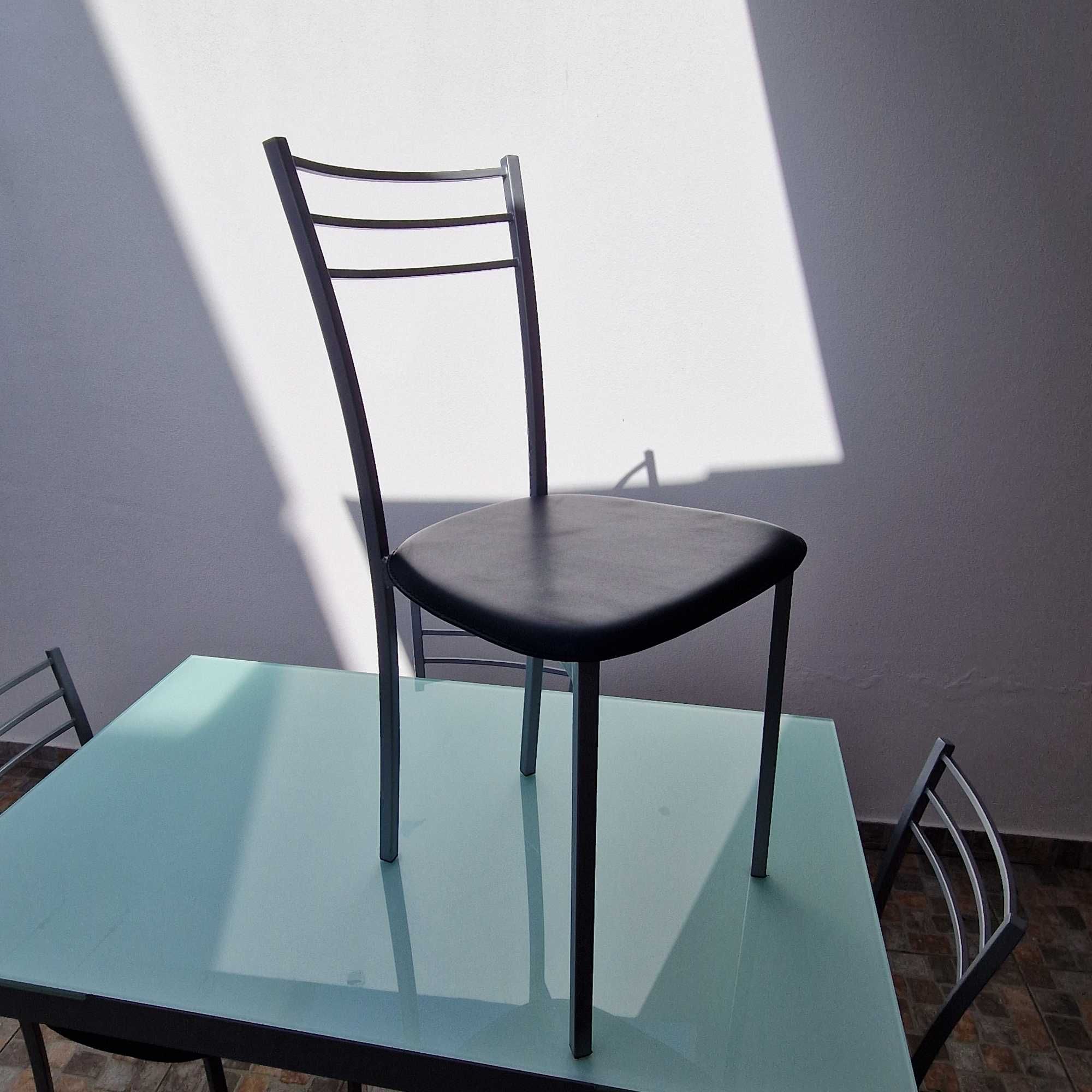 Mesa extensível com tampo em vidro e quatro cadeiras forradas a preto.