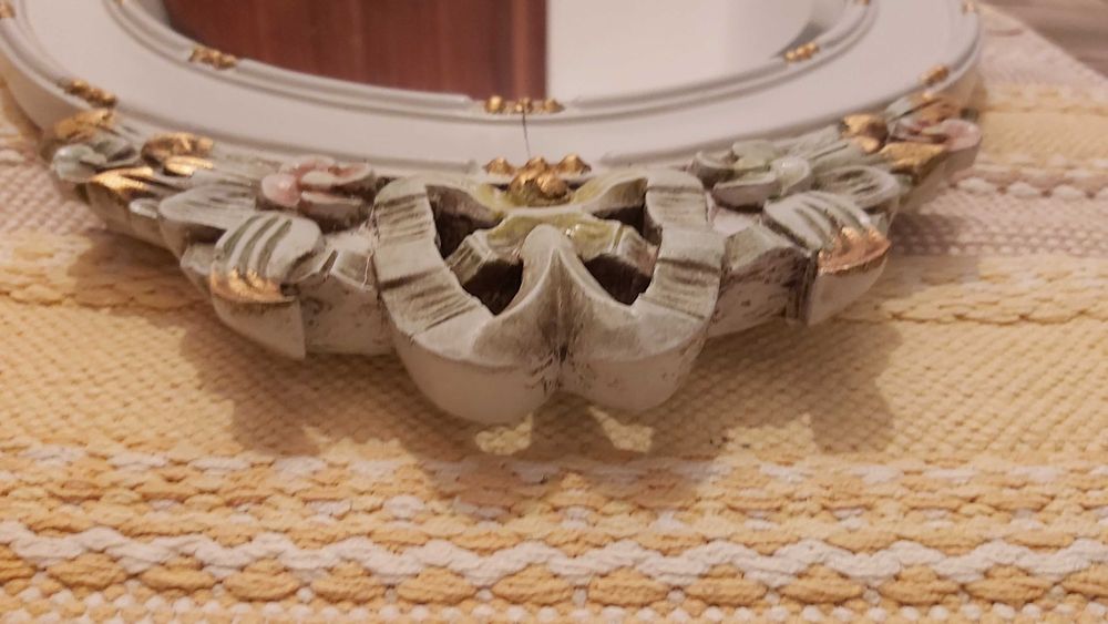 Espelho biselado com moldura de madeira com detalhes esculpidos.