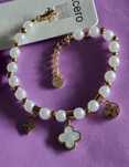 Pulseira dourada, em aço, com pérolas e um trevo branco. Tem extensor
