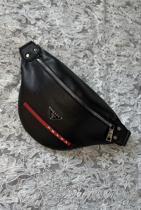 Czarna mała nerka Prada z regulowanym paskiem, zapinana na zamek.