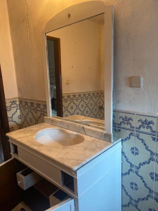 Móvle de casa de banho com tampo em mármore e espelho grande.