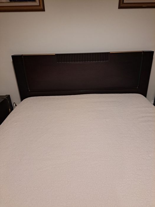 Cama de casal,  cor castanho escuro, com iluminação.