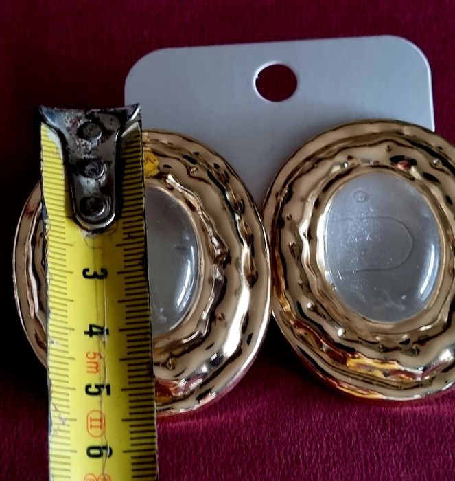 Brincos grandes dourados com acrílico oval transparente no centro.